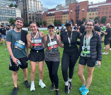 Five team members posing together with race bibs after completing a road race