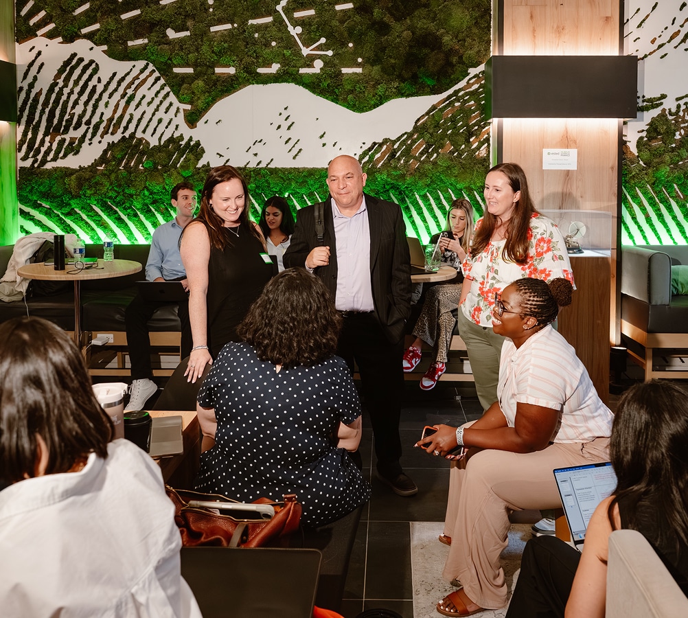 Vested team members mingling and networking in a modern office lounge with a moss wall backdrop